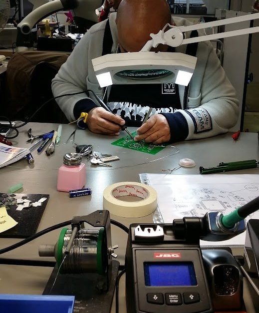 Hand assembly and rework at K9 Electronics' UK facility: an engineer hand-soldering a circuit board under a magnifier lamp with a JBC soldering station.