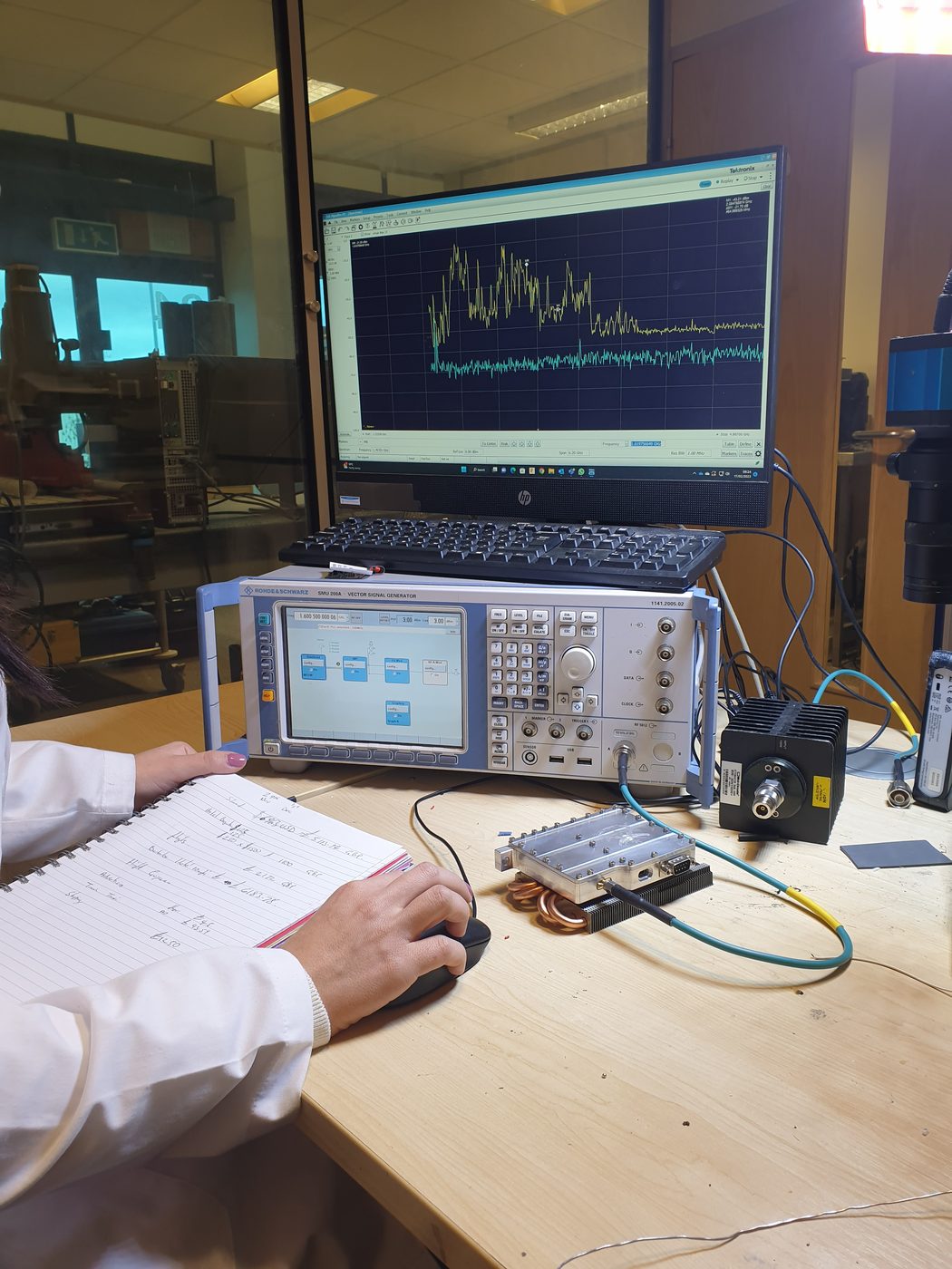 RF test and measurement at K9 Electronics' UK facility: a spectrum analyser trace and a Rohde & Schwarz SMU200A vector signal generator.